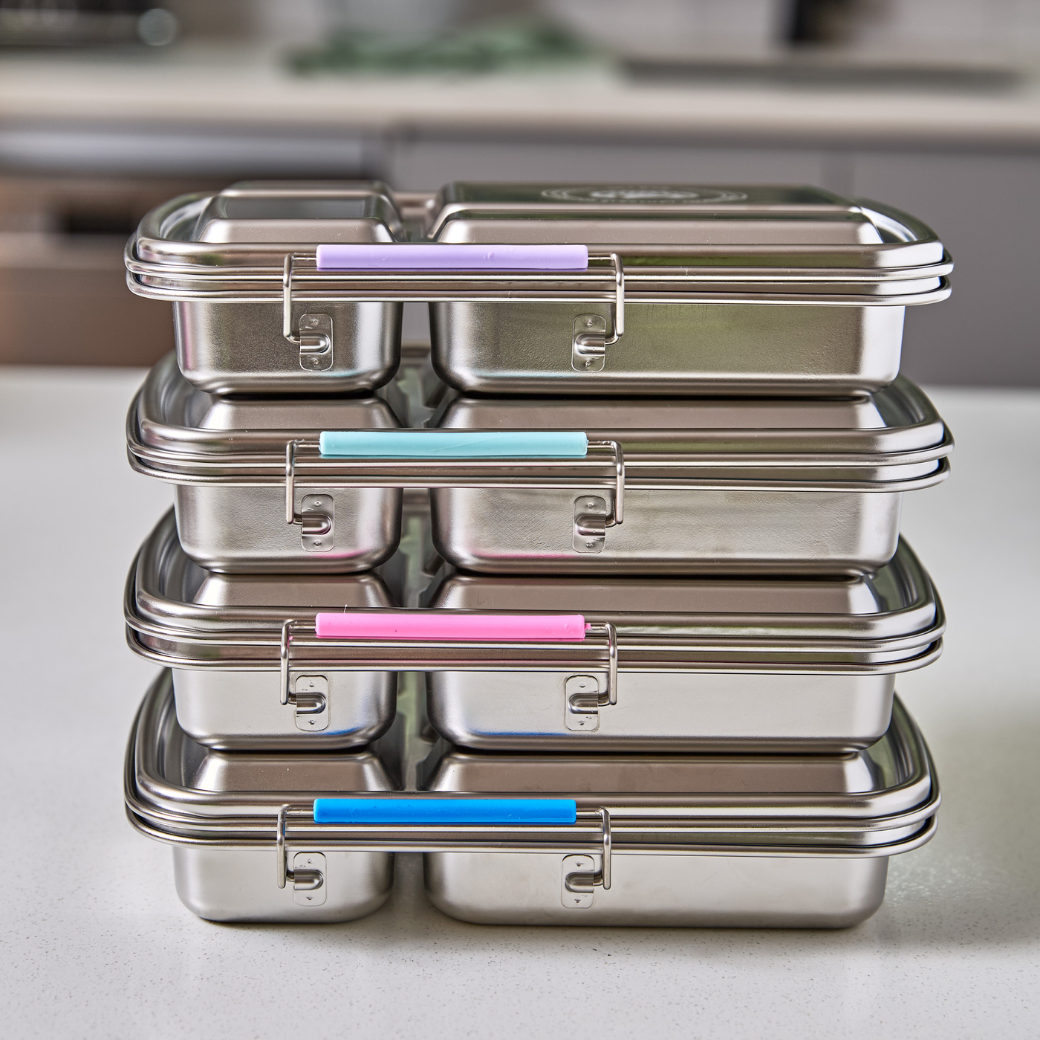 Stack of stainless steel lunch boxes with colored lids on a kitchen counter.