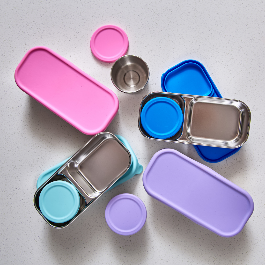 Set of colorful stainless steel containers with lids on a light gray surface