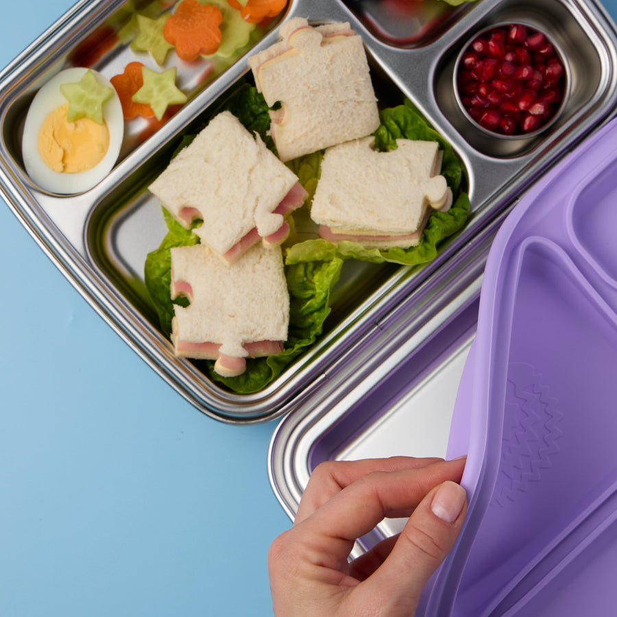 Oli Eve Bento 4 in Jacaranda Mist packed with sandwiches and sides, with the silicone seal being lifted